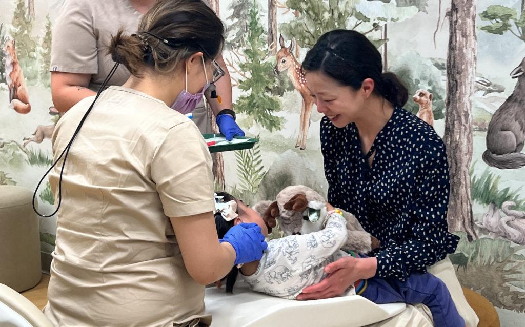 Child at dentist with stuffed animal, smiling mother nearby.