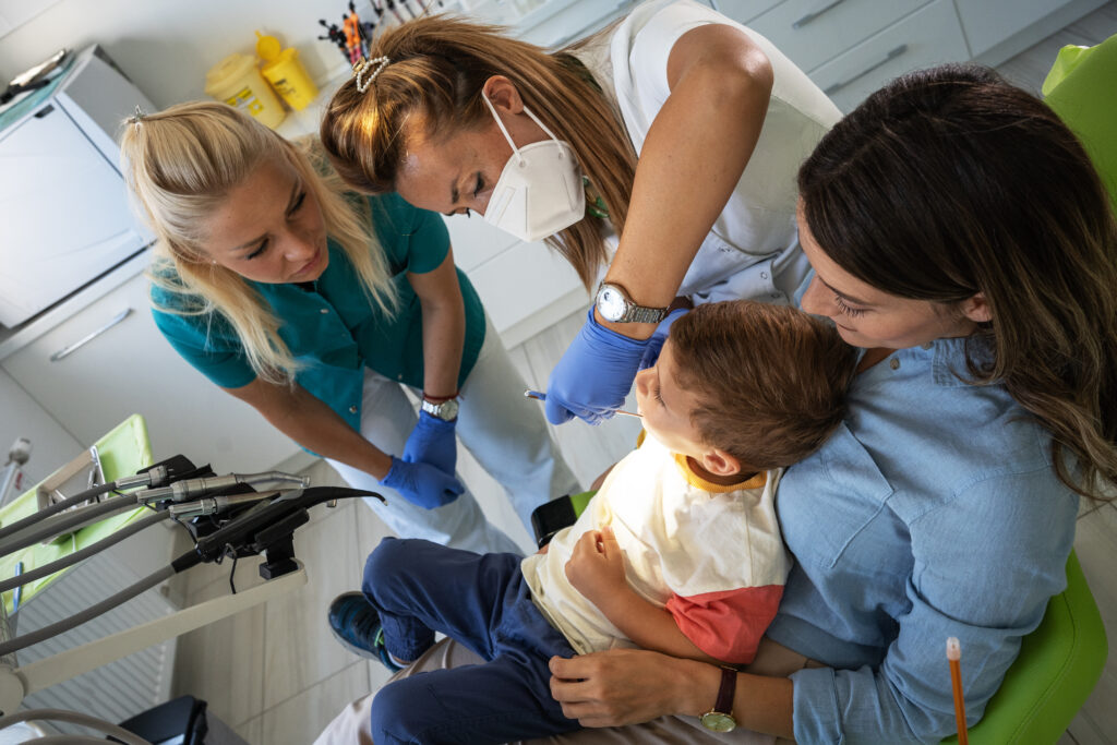 Pediatric dentist performing a gentle knee-to-knee oral exam during a baby’s first preventive dental visit with parent support