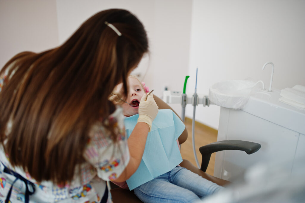 Pediatric dentist gently examining an infant’s teeth while a parent provides comfort during a baby’s first dental visit